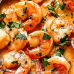 A bowl of Creamy coconut shrimp recipe garnished with cilantro and lime wedges.